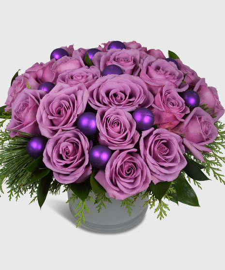 Purple roses, winter greenery and shiney purple balls in a white cylinder vase