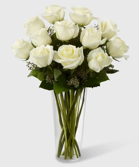 Long stem white roses and greenery in a clear glass vase.