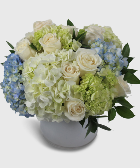 Cream roses, pastel hydrangea and elegant greenery in a white cylinder vase.