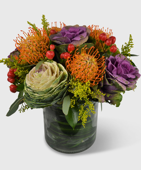 Fall bouquet designed in a leaf-lined vase with orange pincushion protea, purple and green kale, orange hypericum with nice fillers and green