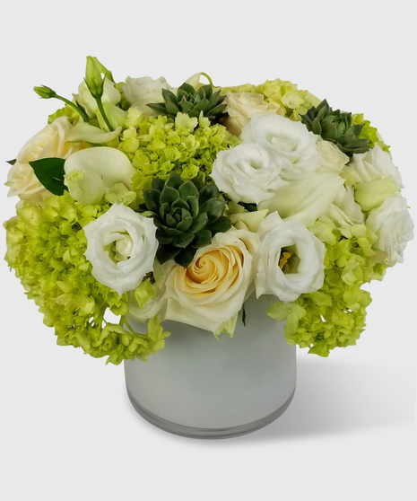 Ivory, cream & green flowers with lush greenery in a cylinder vase.