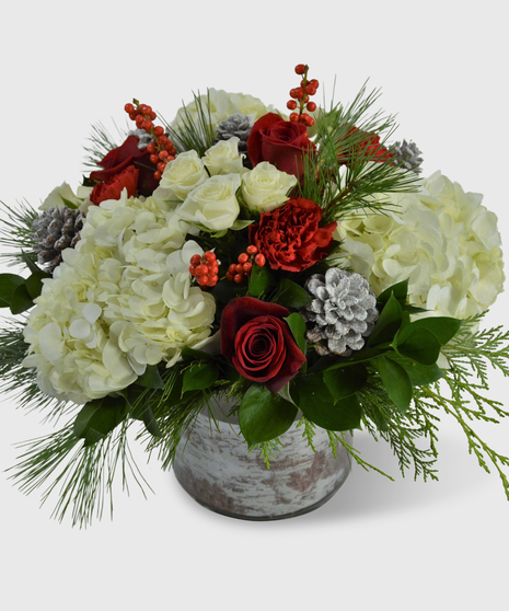 Red and white flowers and holiday greens designed in a birch-lined vase