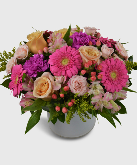 Pink, purple and peach flowers designed in a short white cylinder vase