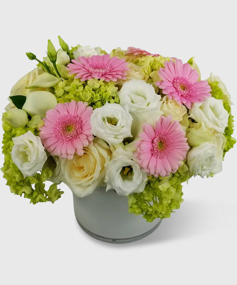 Light pink, white, creme and green flowers designed in a white cylinder vase