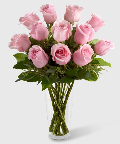 Pink roses and greenery in a clear glass vase.