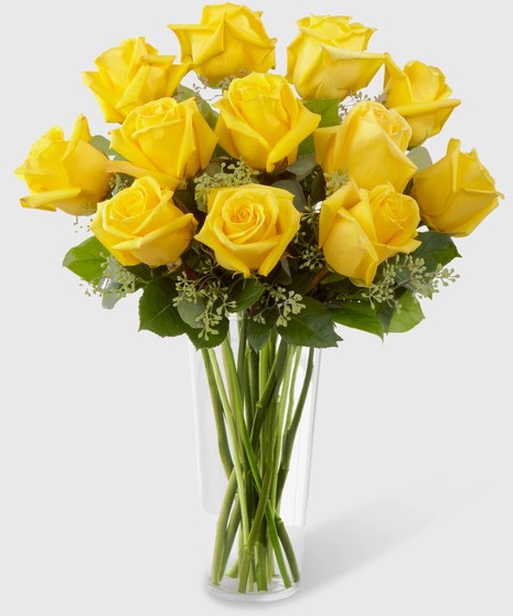 Long stemmed yellow roses with seeded eucalyptus in a clear glass vase.