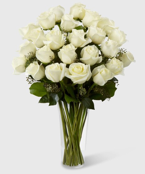 Long stem white roses and greenery in a clear glass vase.