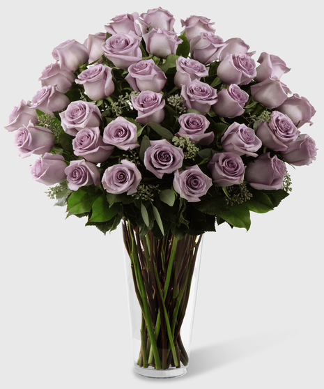 Long stem purple roses and seeded eucalyptus in a stylish glass vase.