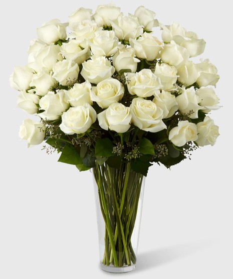 Long stem white roses and greenery in a clear glass vase.