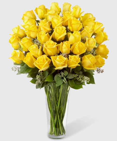 Long stemmed yellow roses with seeded eucalyptus in a clear glass vase.