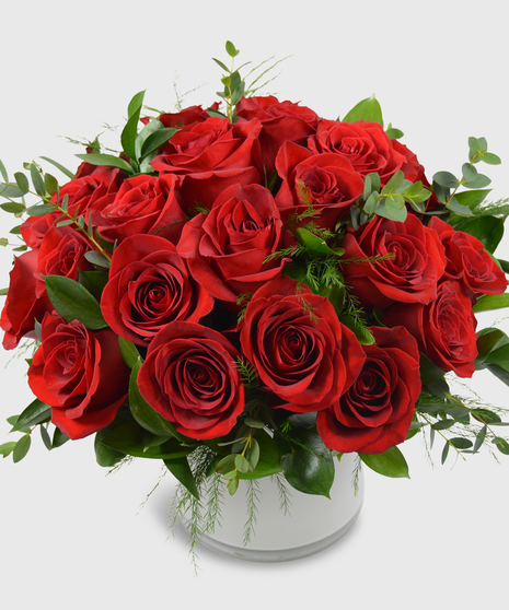 Red roses designed in a short white cylinder with a assorted greenery-Two dozen red roses shown