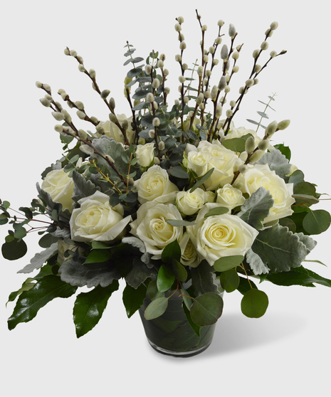 Lush greenery with white roses and white spray roses in a leaf-lined vase.