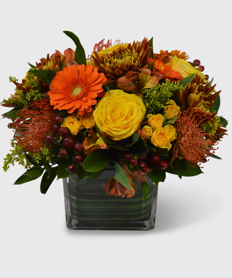 Bronze mums, orange mini gerbera, yellow roses, brown berries and more designed in a leaf-lined block vase