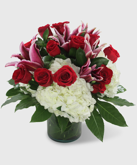 Red roses, white hydrangea, pink lilies and tropical greenery in a leaf-lined vase.