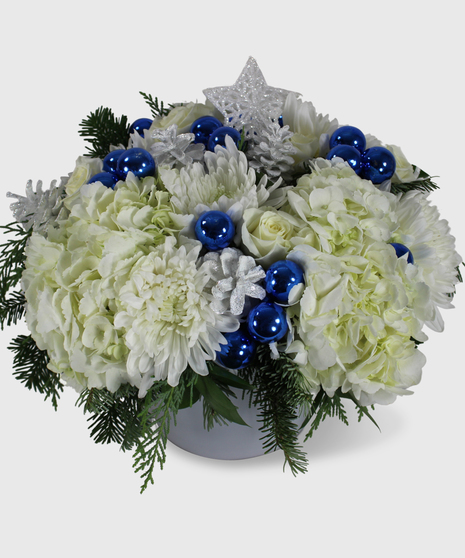 A blue and white holiday arrangement in a white cylinder vase