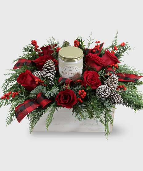 A winter centerpiece of red flowers, ribbons and pinecones in a white wooden box adorned with a white candle