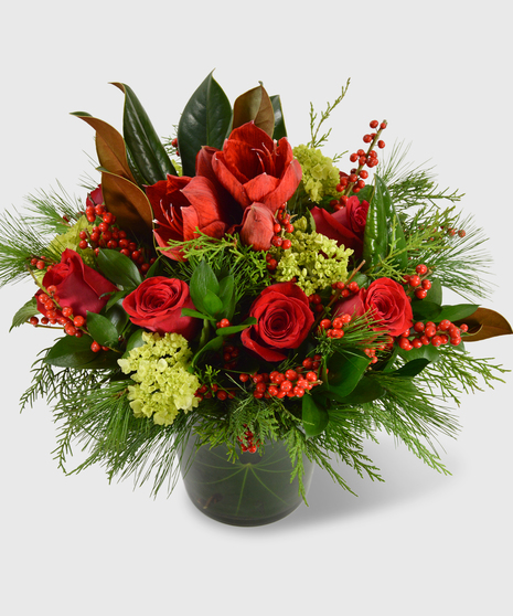 A lush vase filled with winter greens, magnolia leave and bright red flowers