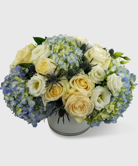 White, blue and creme flowers designed in a short white cylinder vase