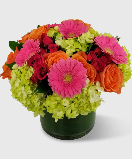 Orange roses, green hydrangea, pink spray roses and more in a leaf linfed vase.