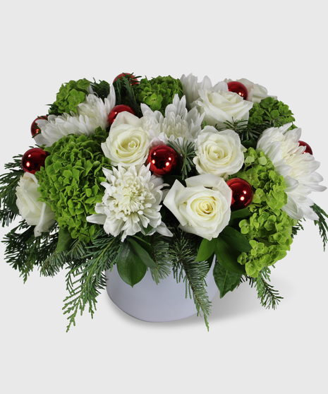 White and green flowers, winter greens and red shiney balls designed in a white cylinder vase