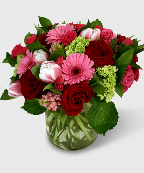 Red roses, tulips, hyacinth and more in a cylinder vase.