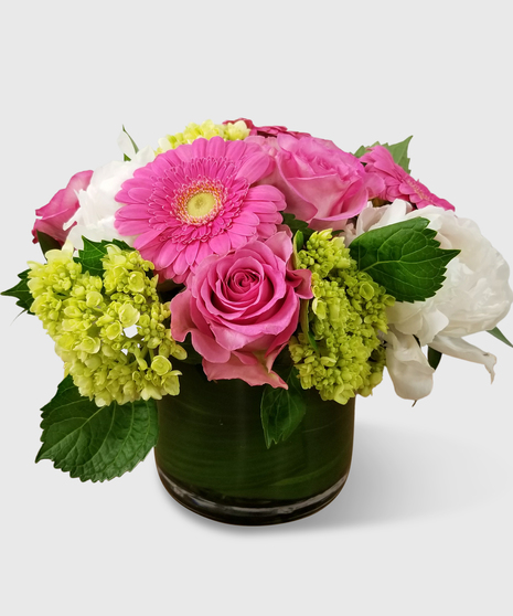 Pink peonies, pink roses, mini green hydrangea and pink gerbera daisies in a leaf-lined cylinder vase.