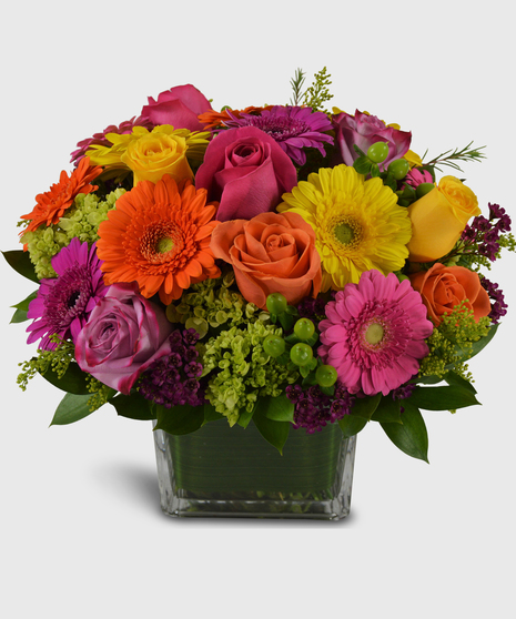 A bright mix of colorful roses, colorful mini gerbera, green hydrangea and hypericum designed in a heavy leaf-lined block vase