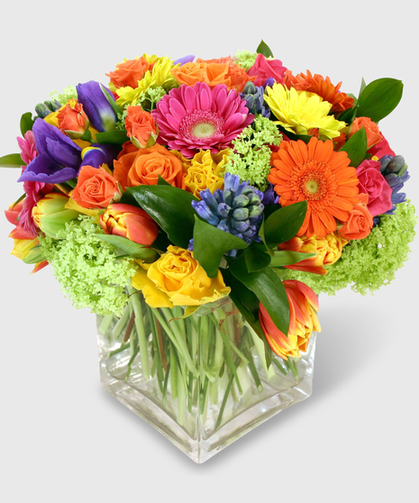 Hyacinths, tulips, iris and gerbera daisies in a clear glass block vase.