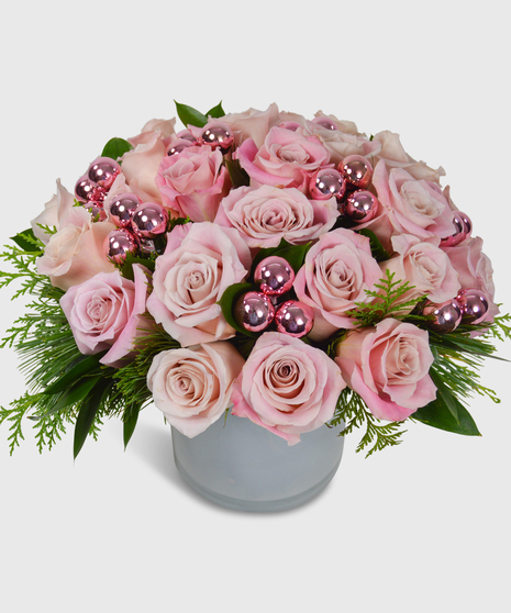 Soft pink roses, pink shiney balls and holiday greens in a white cylinder vase